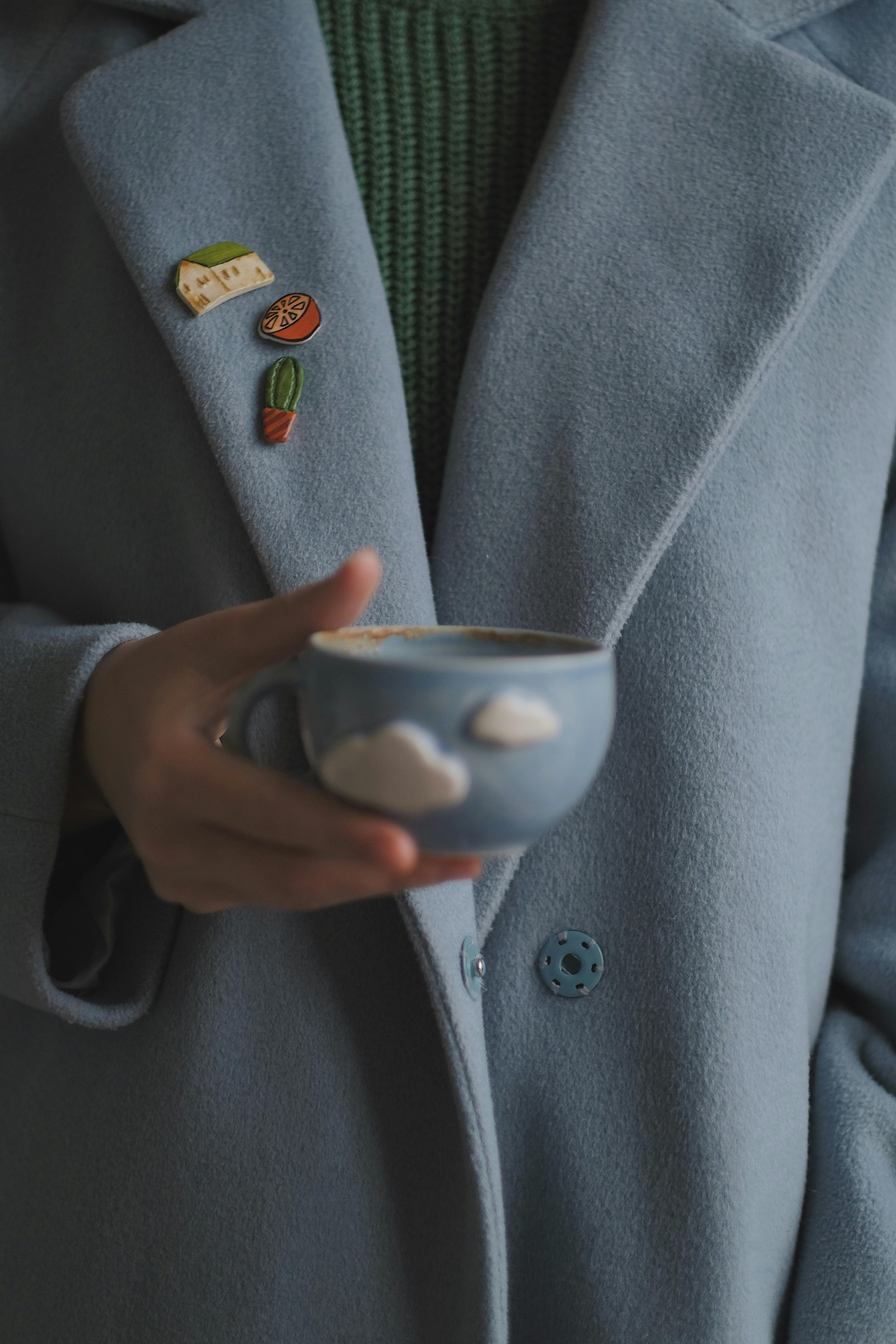 A person in a blue coat holds a cloud-decorated cup, exuding warmth and style.