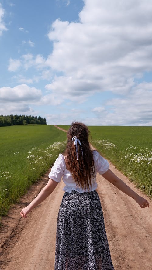 Free A Back View of a Woman in Floral Skirt Standing Between Green Grass Field Stock Photo