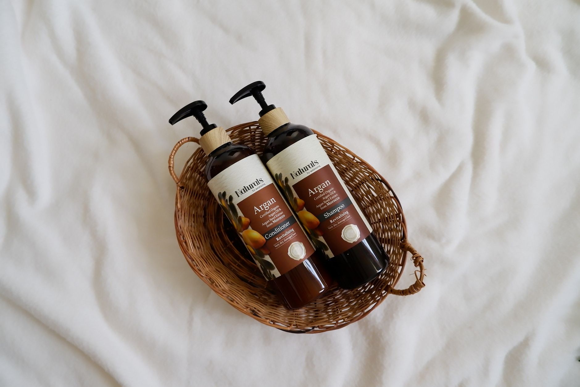 Overhead view of natural argan oil shampoo and conditioner in a wicker basket.
