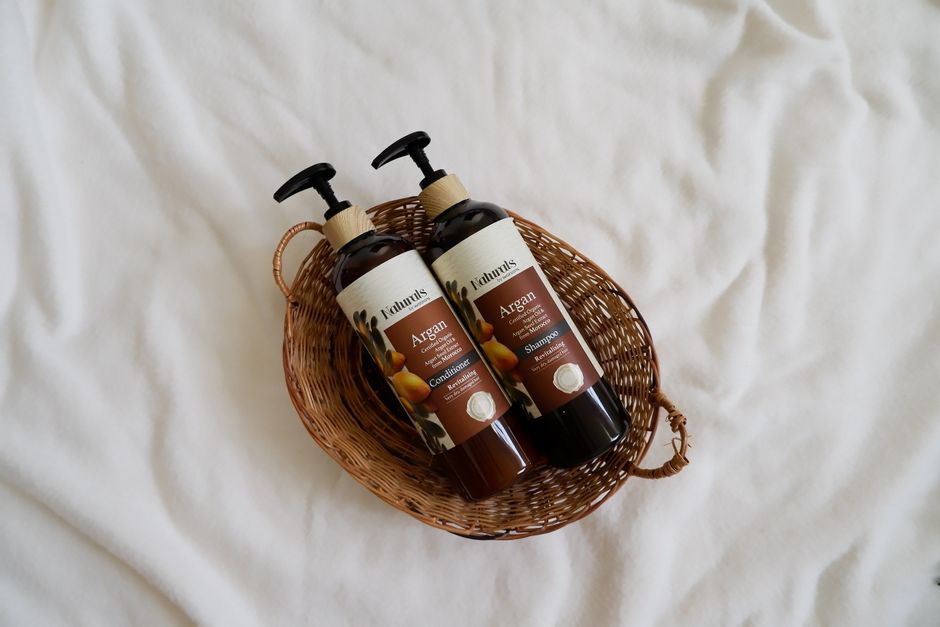 Overhead view of natural argan oil shampoo and conditioner in a wicker basket.