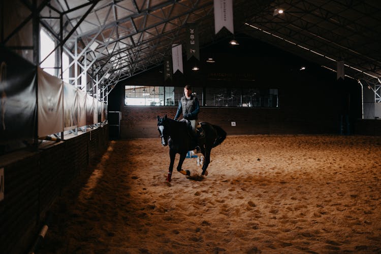 A Man Riding A Horse In An Indoor Arena