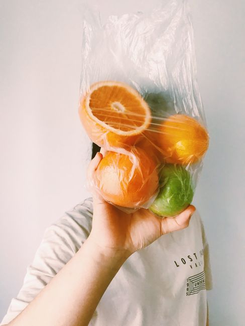 A hand holding a plastic bag filled with citrus fruits, obscuring the face for a creative effect.