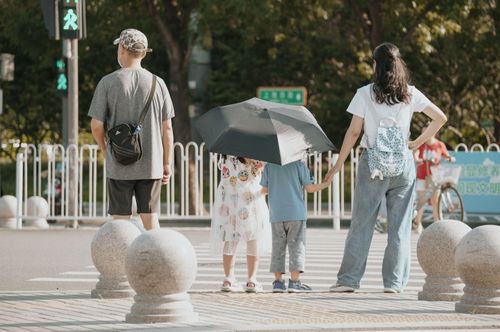 Free A family waits at a crosswalk with children holding an umbrella on a sunny day. Stock Photo