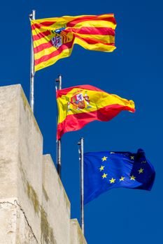 Flags of Aragón, Spain, and Europe waving on a pole under a clear blue sky.