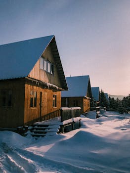 Charming wooden cabins covered in snow during a sunny winter day, serene ambiance.