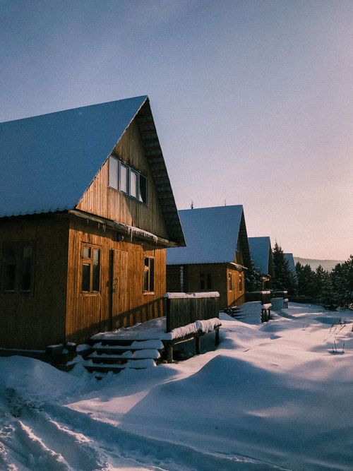 Free Charming wooden cabins covered in snow during a sunny winter day, serene ambiance. Stock Photo