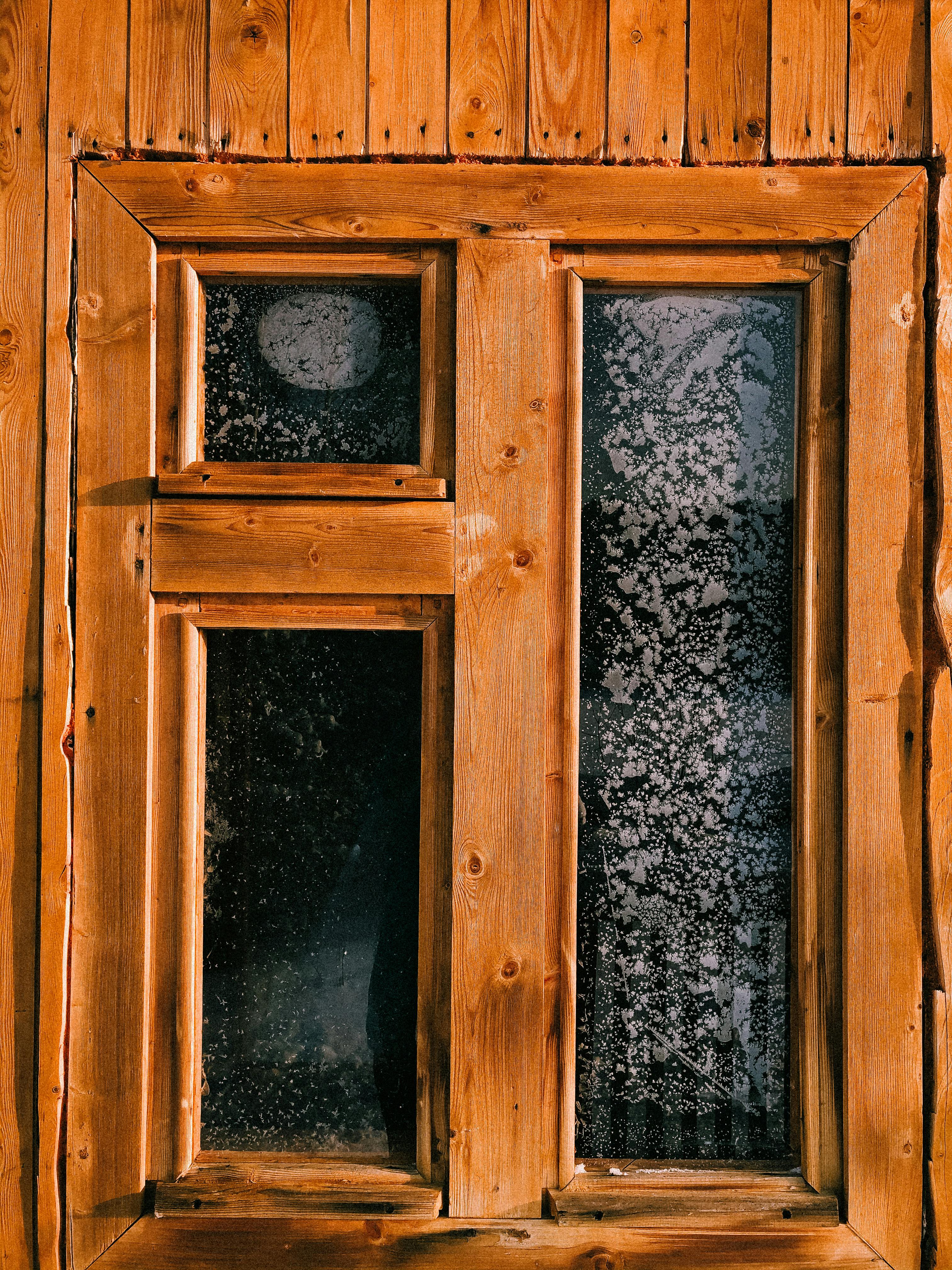 A rustic wooden window with frosted glass panels, showcasing a textured winter scene.