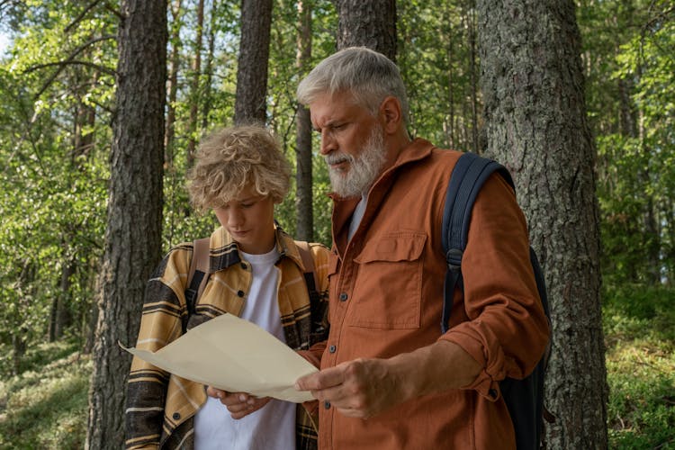 Grandfather And Grandson With Map During Hiking Through Forest