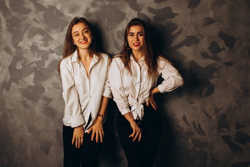Women in White Long Sleeves Smiling while Leaning on the Wall