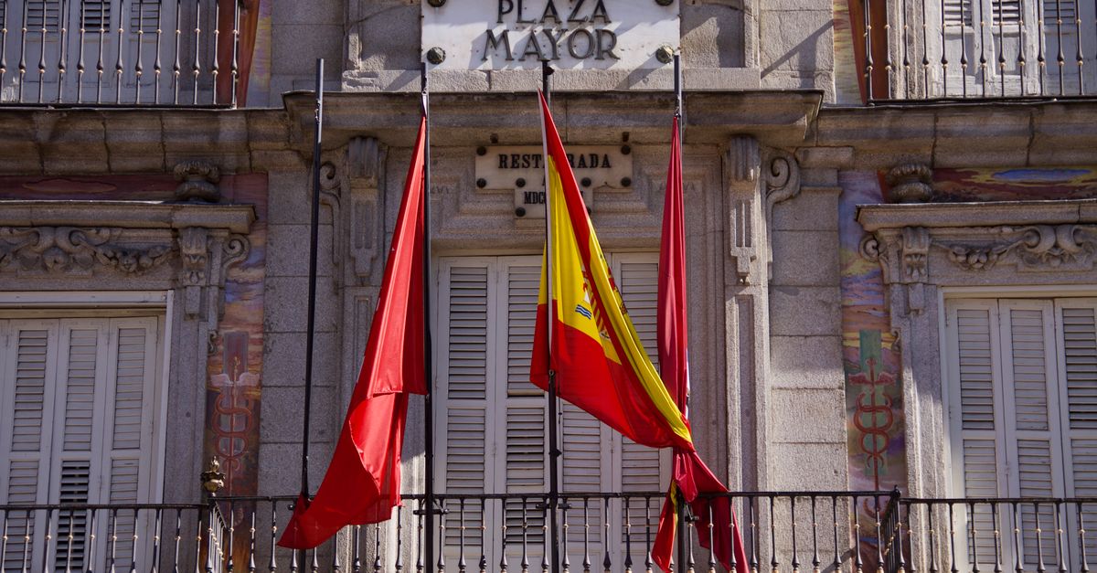 Vista detallada de la fachada de la Plaza Mayor con banderas en Madrid, España, resaltando la arquitectura clásica.