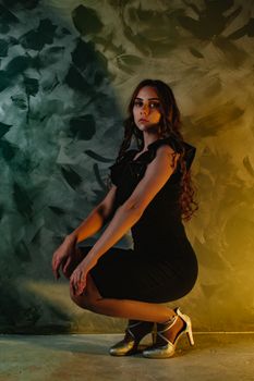 Elegant woman posing in a stylish black dress against an artistic backdrop, showcasing fashion and style.
