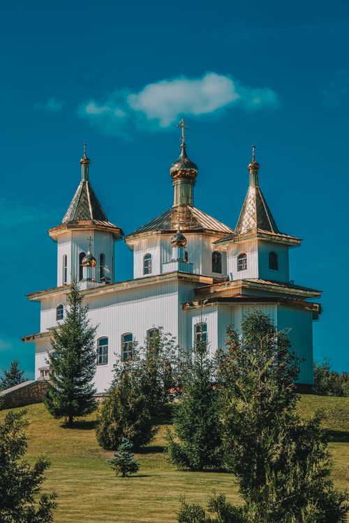 Free A beautiful church with golden domes situated on a lush hill under a bright blue sky. Stock Photo