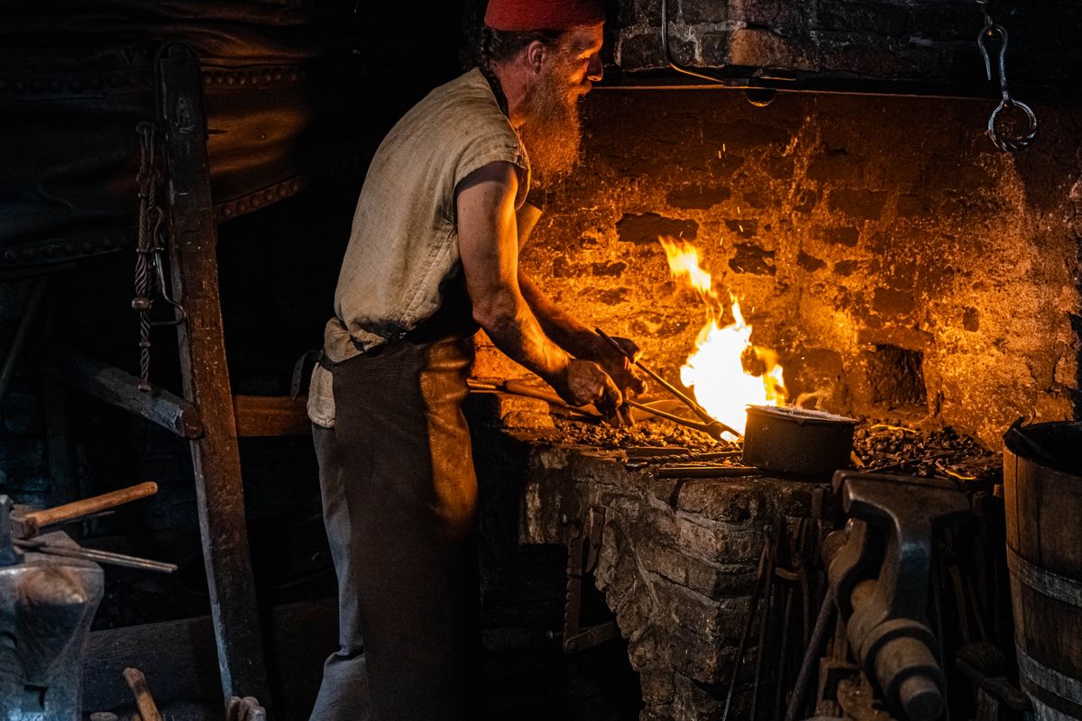 Fierar care modelează o piesă de metal într-o forjă cu lumină slabă