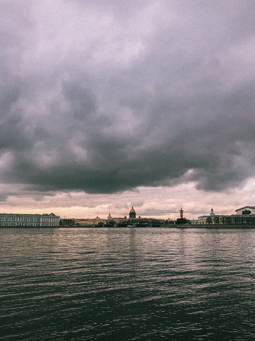 Free Scenic view of St. Petersburg skyline under dark, moody clouds across a calm river. Stock Photo