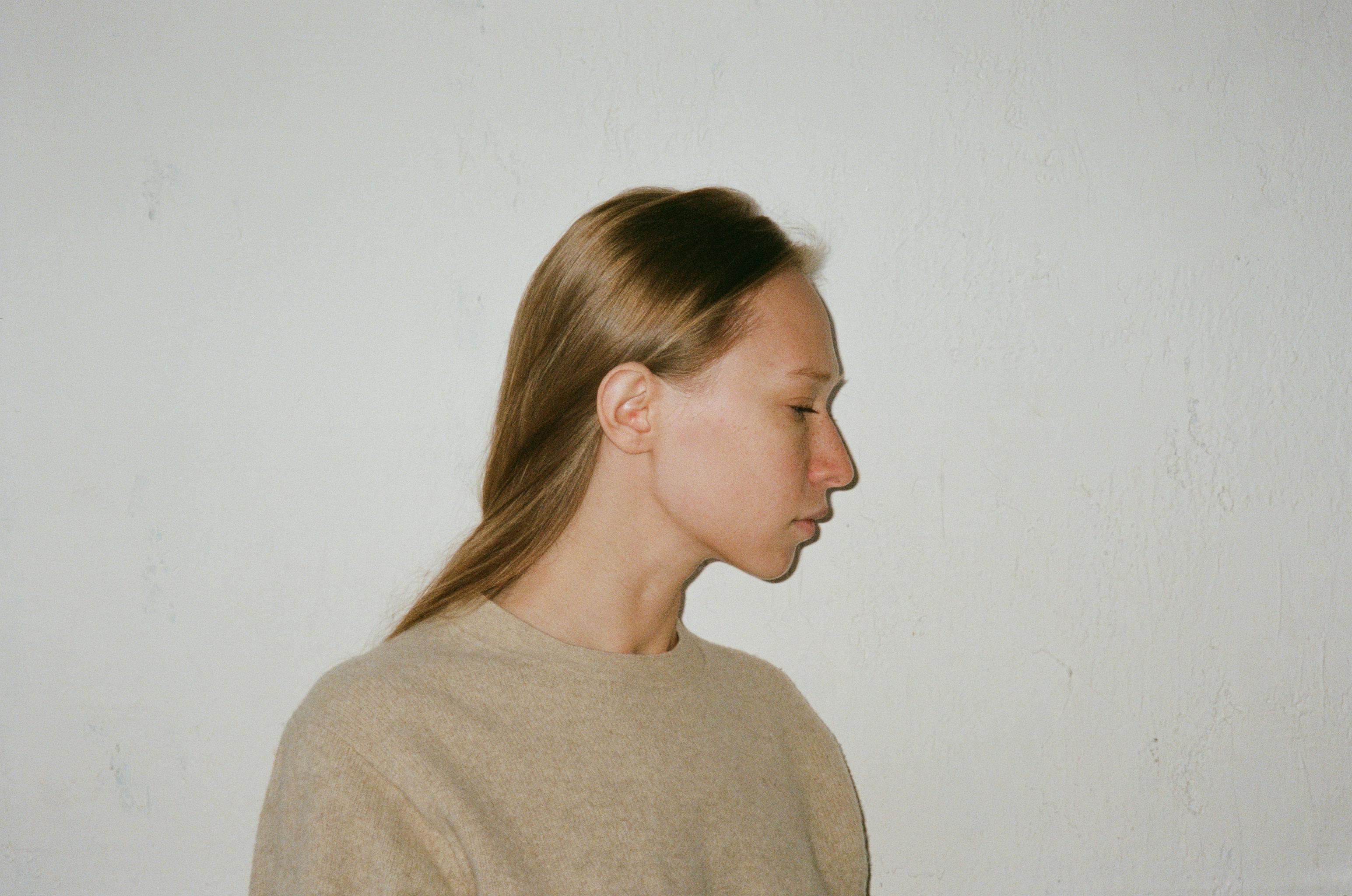 A serene side profile of a woman against a textured beige wall.
