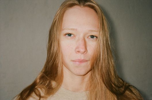 A serene close-up portrait of a woman with blond hair and freckles indoors.