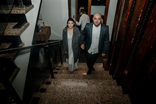 Man and Woman Holding Hands While Going Up the Stairs
