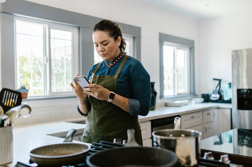 Free Woman Using Smart Phone in Kitchen Stock Photo