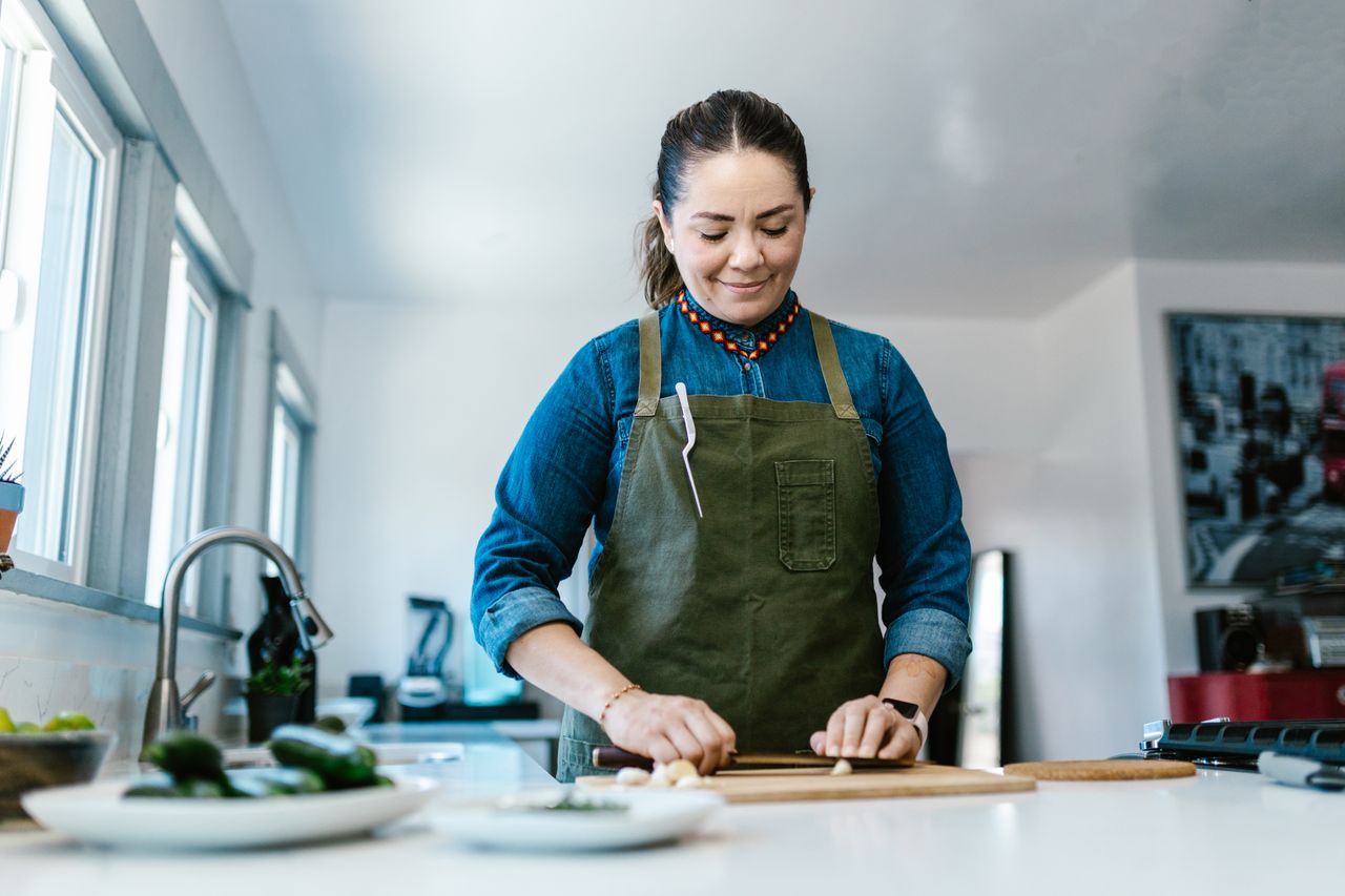 woman in a kitchen chopping vegetables on a cutting board wearing a gr