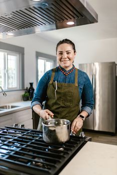 Smiling woman cooking a meal on a stove in a modern kitchen.
