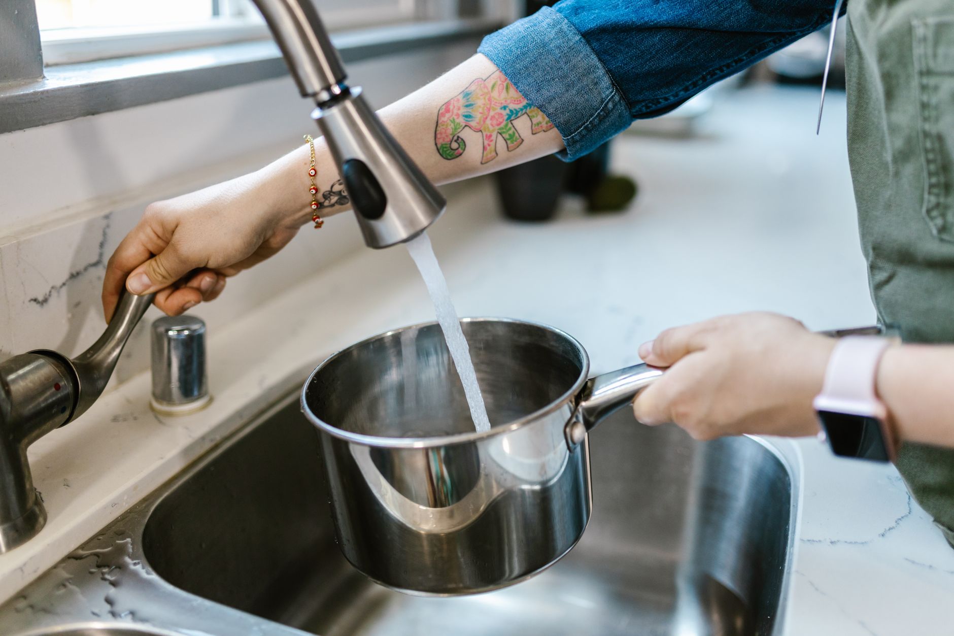 Close-up of adult hands filling a pot with tap water in a kitchen sink.