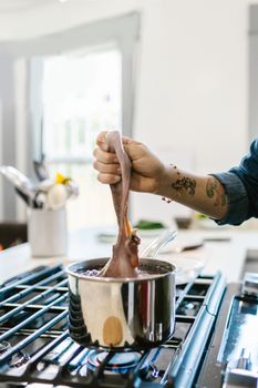 A hand with tattoos lowers octopus into a stainless steel pot on a stove, preparing seafood indoors.