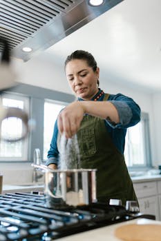 A woman seasoning food while cooking at home in a modern kitchen.
