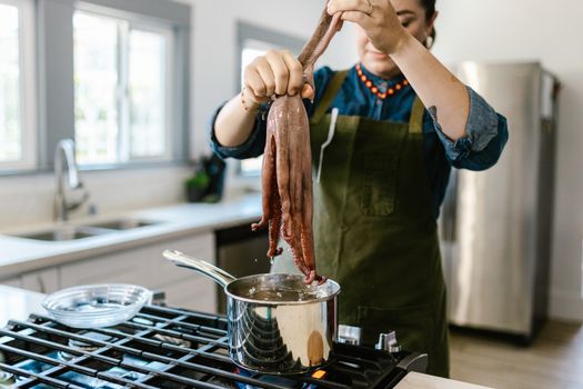 A woman prepares octopus on a stove in a contemporary kitchen setting.