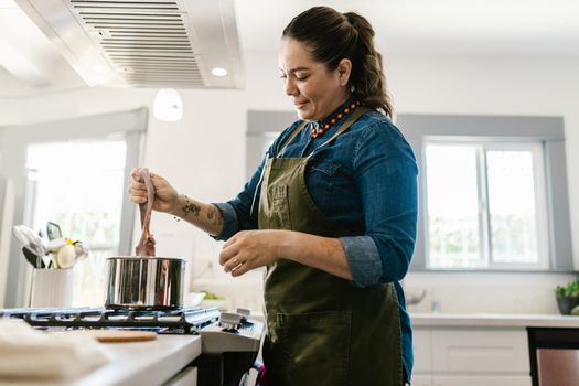 A woman in an apron expertly cooks octopus on a stovetop in a bright, modern kitchen.