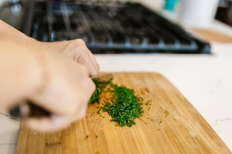 A Person Chopping Chives On A Wooden Cutting Board