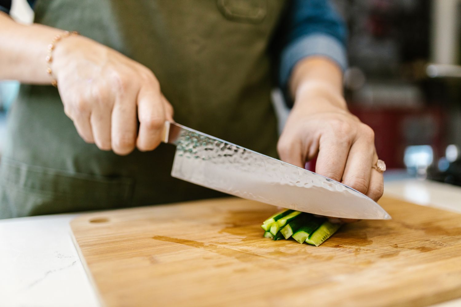 Chef knife slicing green vegetables on a wooden cutting board