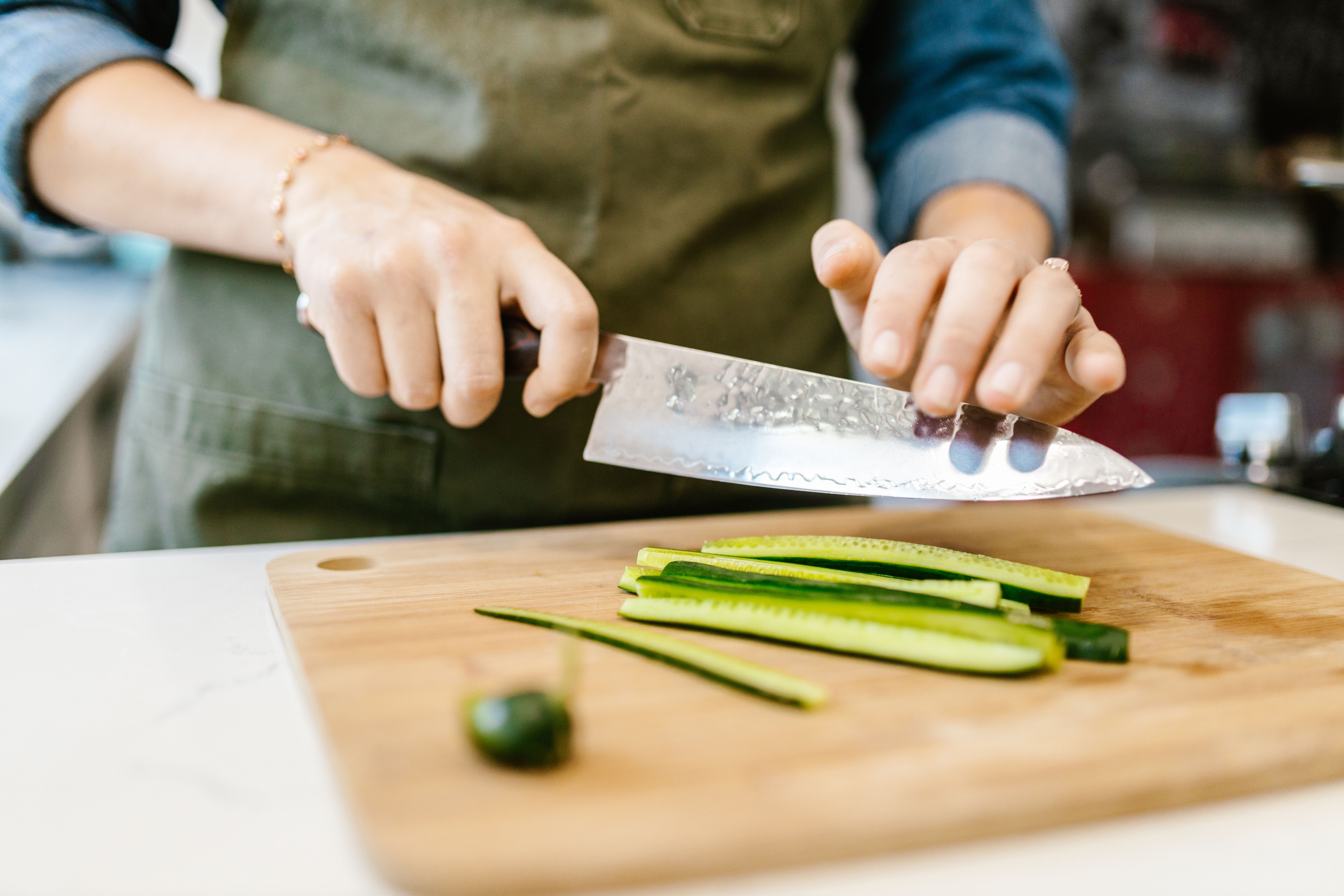 Close-up of a woman slicing cucumber on a cutting board indoors. Fresh vegetables and cooking concept.