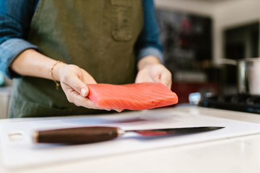 A person holds a fresh salmon fillet in a kitchen setting, ready for preparation.