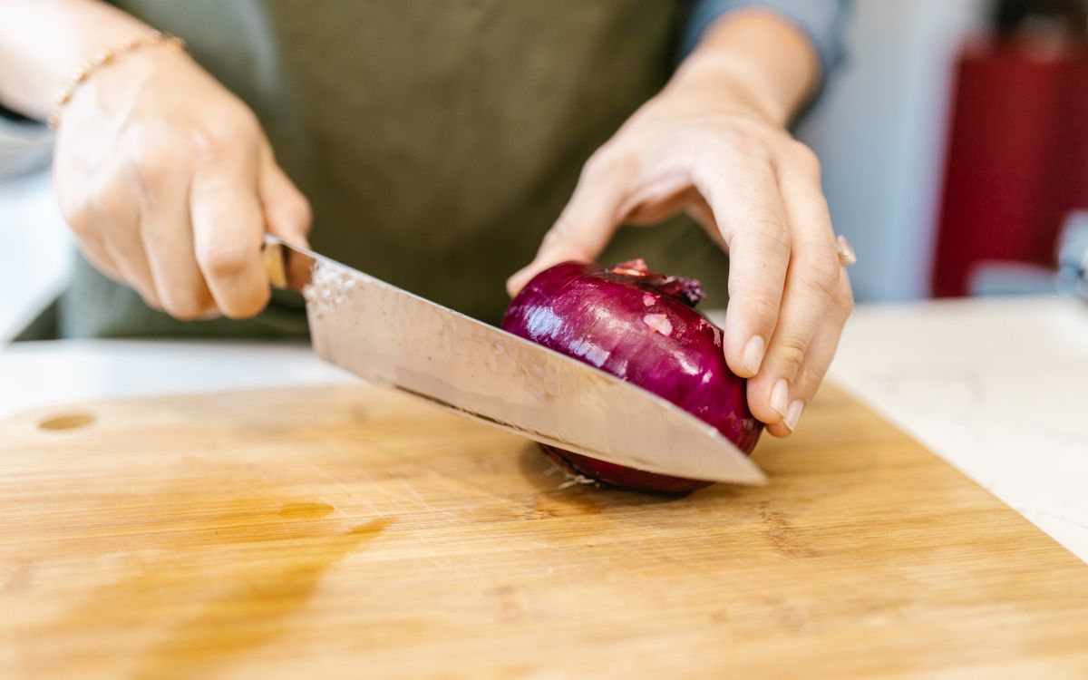 Close-up of hands cutting a red onion on a wooden board indoors.
