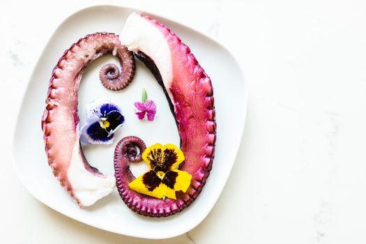 A gourmet dish featuring octopus tentacles and colorful edible flowers on a white plate.