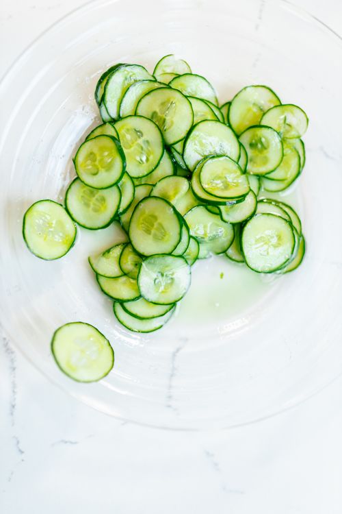 Top-down view of fresh cucumber slices arranged in a transparent bowl on a white background