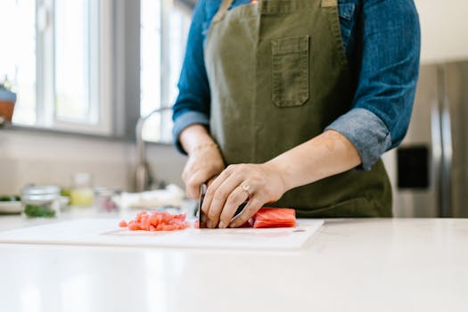 Woman chopping fresh salmon fillet on a kitchen counter indoors, showcasing cooking skills.