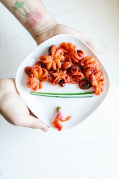 Freshly grilled octopus served on an elegant white plate with artistic garnishes, held by a tattooed hand.