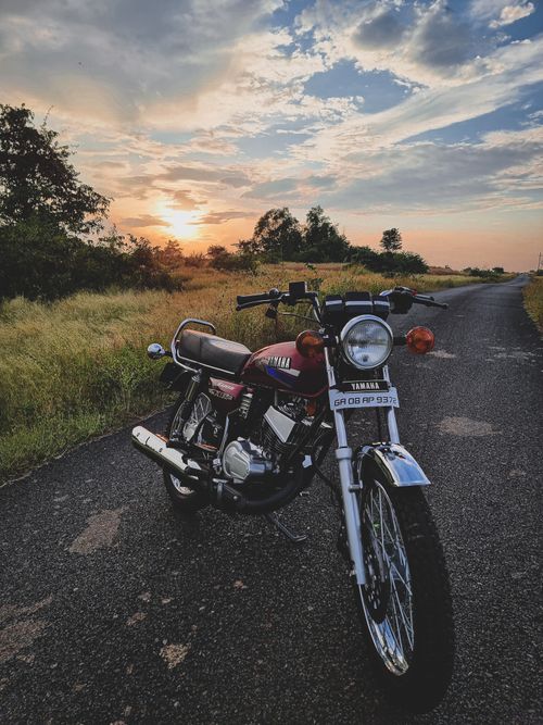 Free A classic motorcycle parked on an empty rural road in India during sunset, showcasing serene and adventurous travel vibes. Stock Photo