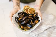 Hands Holding Oyster Based Gourmet Dish in White Plate