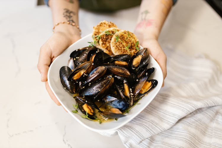 Hands Holding Oyster Based Gourmet Dish In White Plate