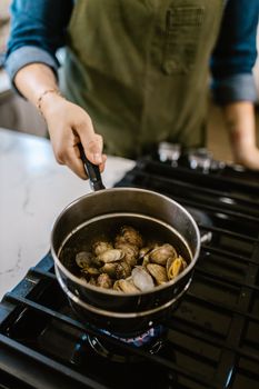 A person cooking clams in a pot on a stove in a modern kitchen.