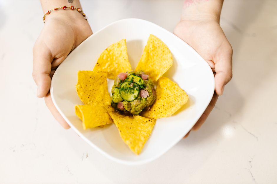 A molcajete filled with chunky green guacamole, flecked with diced red onion and cilantro, with a lime wedge and tortilla chips on the side.