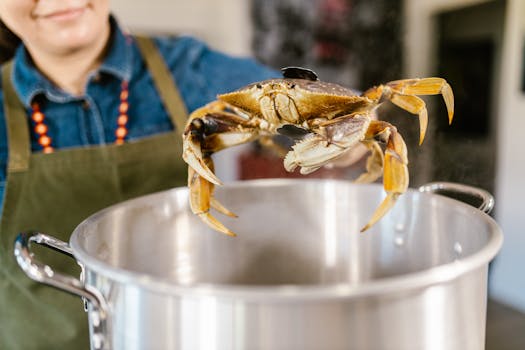 Close-up of a chef holding a crab over a boiling pot, ready for cooking.