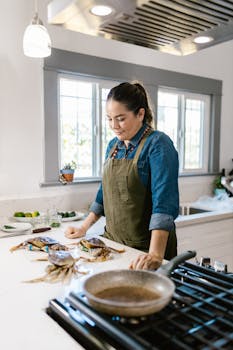 Woman in kitchen prepping fresh crabs at a counter, bright indoor setting.