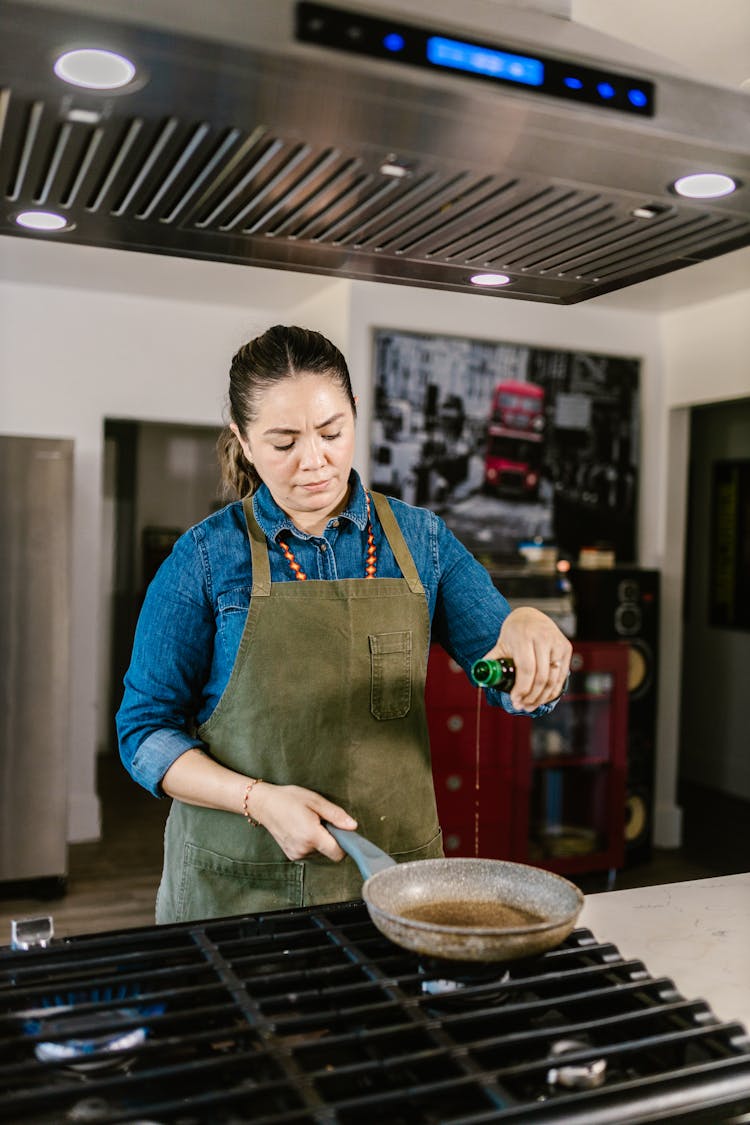 Female Chef In Apron Pouring Oil On Frying Pan 