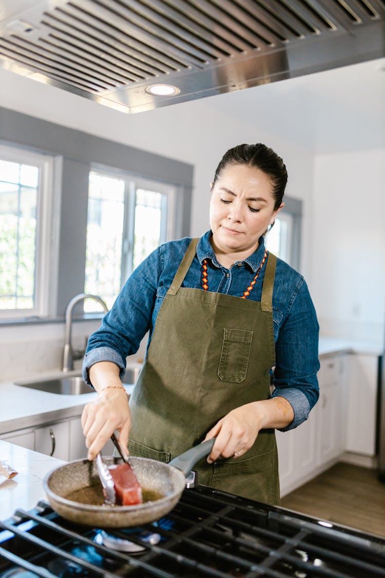 Woman Turning Tuna Meat On Frying Pan Standing On Cooker