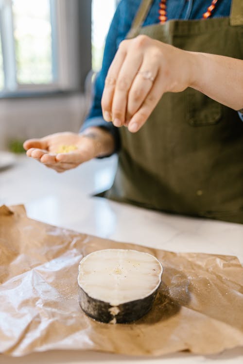  Chefs Hand Sprinkling Spices on Fish Slice Laying on Wrapping Paper