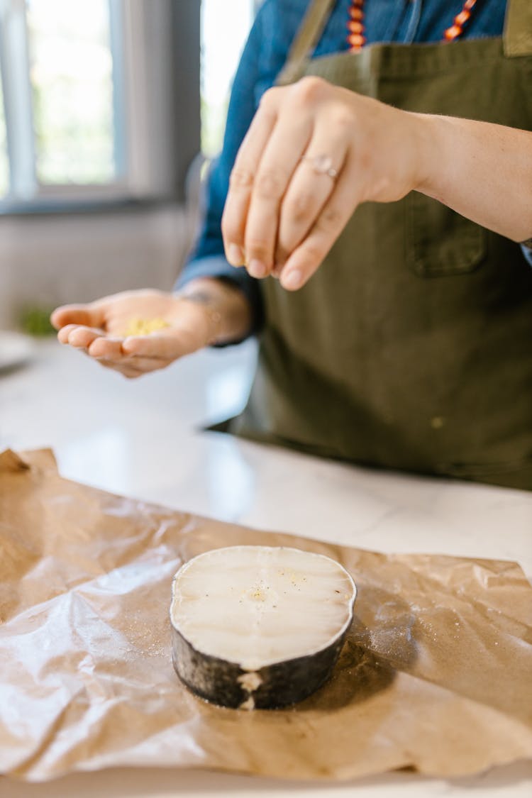  Chefs Hand Sprinkling Spices On Fish Slice Laying On Wrapping Paper