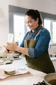 A woman in an apron seasons a salmon fillet in a modern kitchen, showcasing culinary skills and fresh preparation.